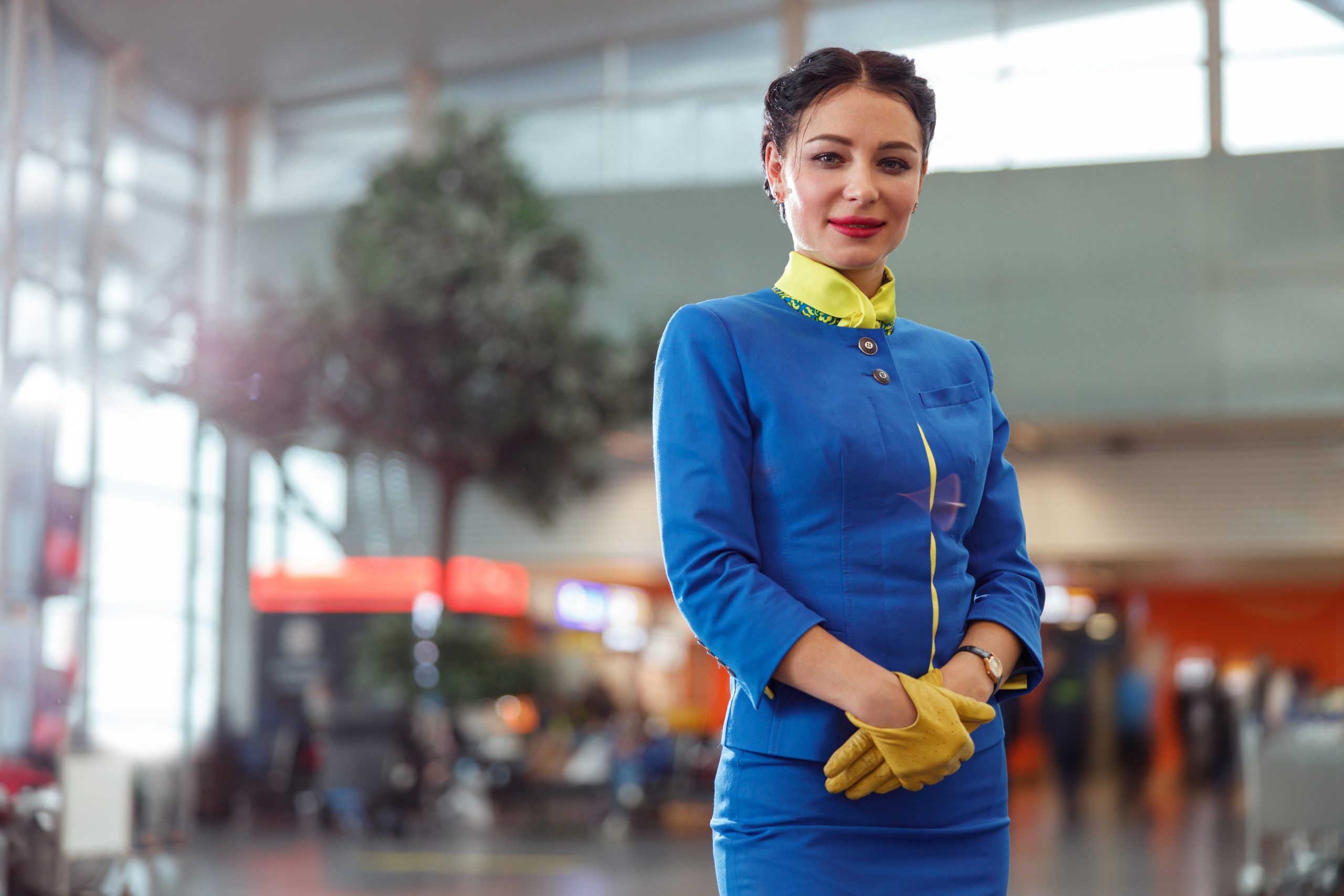 Female air hostess or stewardess wearing blue aviation uniform and gloves while looking at camera and smiling